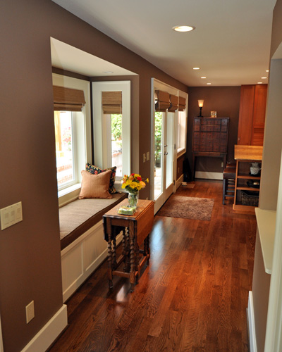 At the main level, a floor plan that formerly dead-ended at a stairwell to the basement is now a circular floor plan, with a space gallery.  The main floor bumpout allowed not only a hall connecting the kitchen and media room, but also a quaint and comfy bay, which doubles as an eating nook.  The built-in cabinetry has a lifting bench seat for storage, and looks out on the newly landscaped backyard