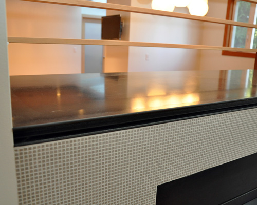 The new cap for the fireplace is polished, blackened steel with a C-channel detail in front. The teeny tiny tile by Brix is about 1/8 x 1/8 inch but has a powerful visual impact on the living room side