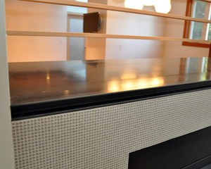 The new cap for the fireplace is polished, blackened steel with a C-channel detail in front. The teeny tiny tile by Brix is about 1/8 x 1/8 inch but has a powerful visual impact on the living room side