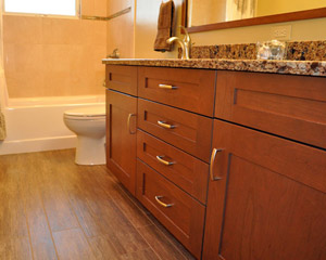 The finished bath benefits from a new window, with sloping sill at the tub.  The previous installation was problematic.  A deco line brightens the tile selection there, complimenting a new acrylic tub.  The porcelain tile floor - Cronin Natif Ginepro - simulates the look of wood, bringing in rich earth tones, tones mirroring the cherry cabinets