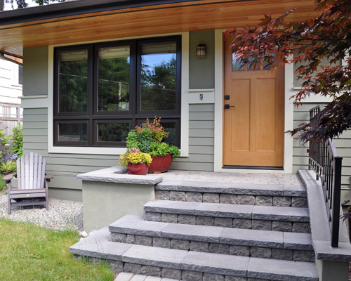 The porch is built with concrete footings, CMU, and finished with pavers and caps, and stucco on the vertical sides.  Stucco in a darker green color is also part of the siding, which includes Hardiplank siding at the lower section, divided by a wood belly band. The new fiberglass entry door and natural wood soffits completes the look